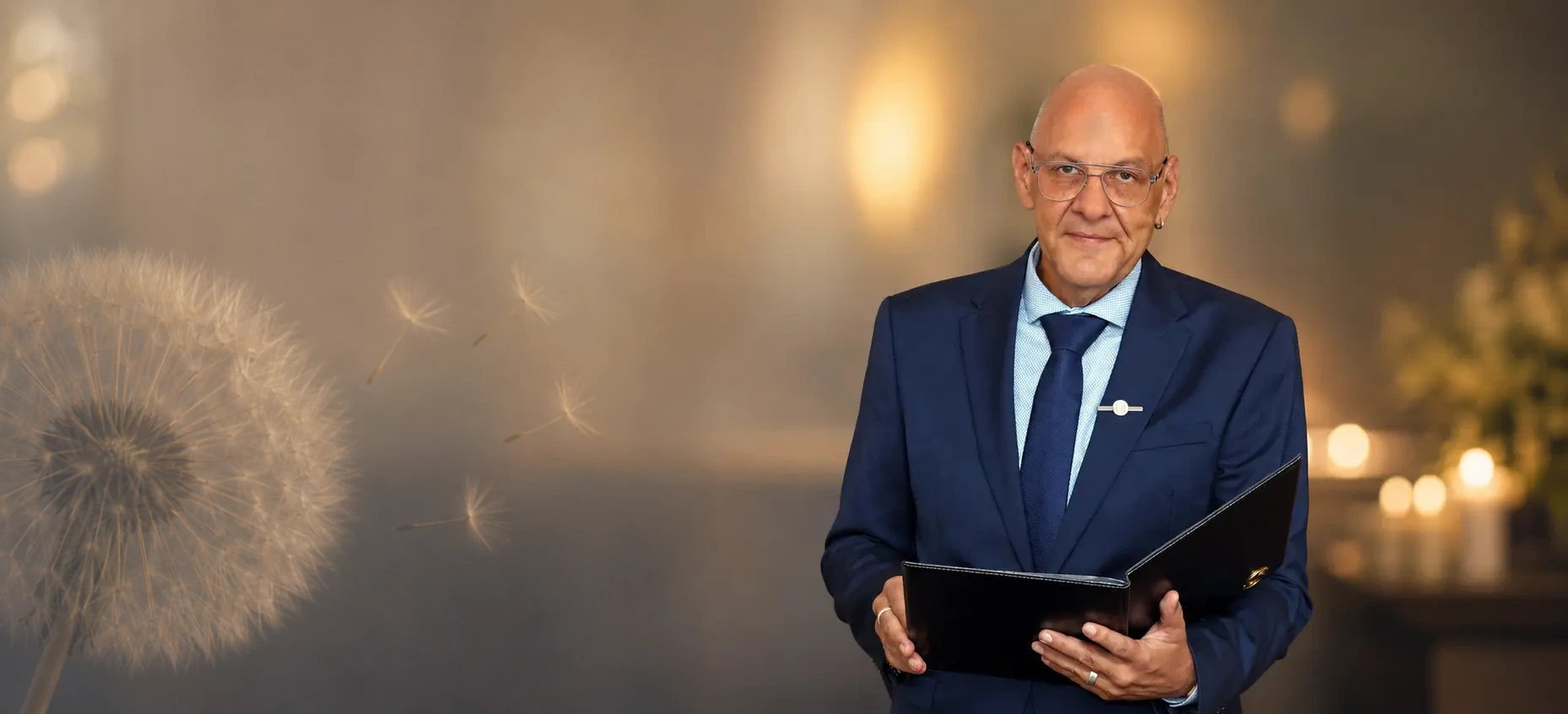 Trauerredner Carsten Riedel mit Redemappe vor warmem, unscharfem Hintergrund und einer dezenten Pusteblume